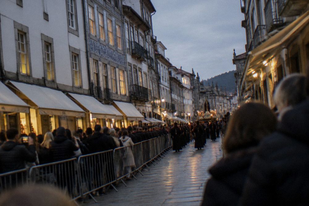 Crowds lined along a pedestrian shopping street waiting behind barriers for a night procession