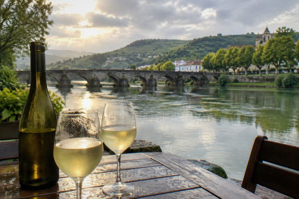 Two chilled glasses of pale vinho verde on a wooden table beside a bottle