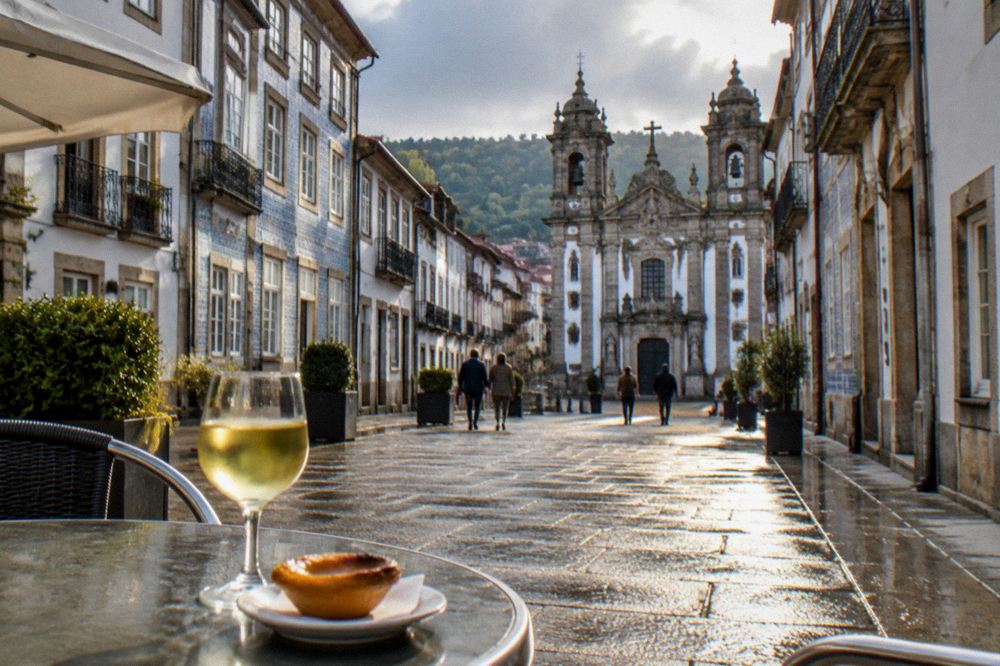 A café table with a glass of vinho verde and a pastry on a sunny Braga square