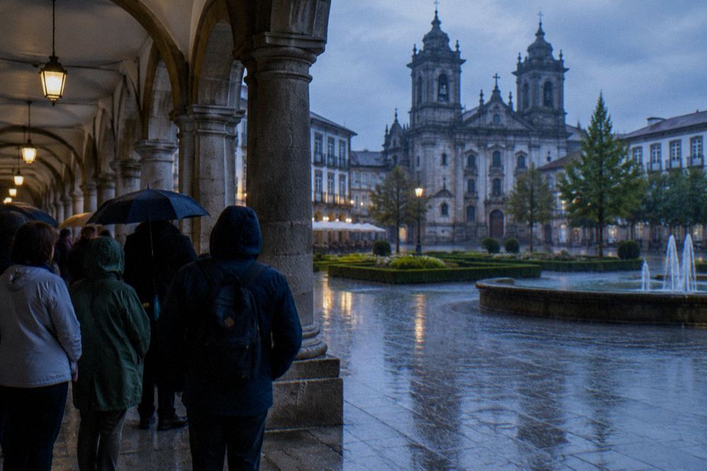 Guided walking group standing under an arcade in Braga while rain falls on the square beyond