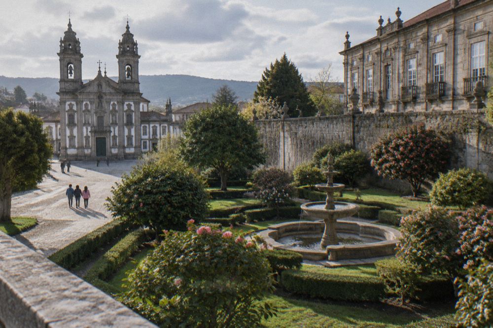 Children looking up at a baroque church facade with twin bell towers from a sunny cobbled square