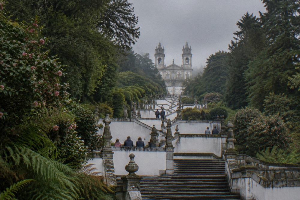 A wide baroque zigzag stairway climbing a wooded hillside with families resting on the landings