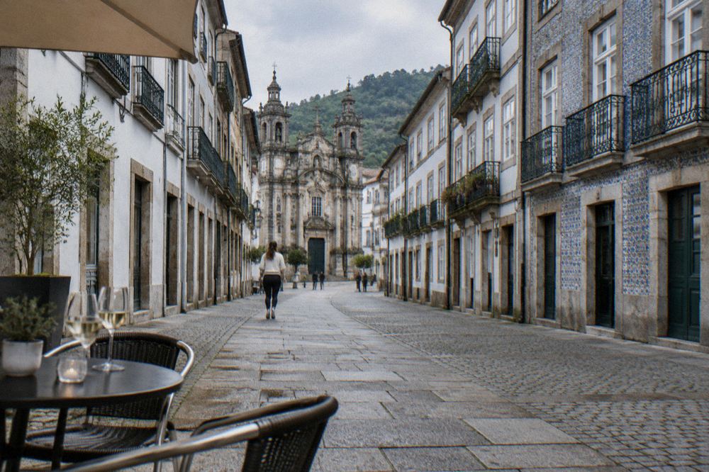An outdoor cafe table with wine glasses set on a cobbled square in Braga